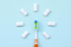 escova de dentes e gomas de mascar estão em um fundo azul pastel. vista superior, postura plana. conceito mínimo foto