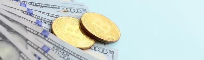 bitcoins dourados e notas de cem dólares estão sobre fundo azul claro foto