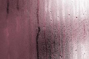 textura de uma gota de chuva em um fundo transparente de vidro molhado. tonificado na cor rosa foto