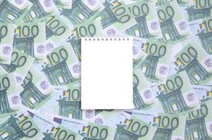 caderno branco com páginas limpas sobre um conjunto de denominações monetárias verdes de 100 euros. muito dinheiro forma uma pilha infinita foto