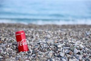 antalya, turquia - 18 de maio de 2021 lata vermelha original da coca cola encontra-se em pequenas pedras redondas perto da costa do mar. coca-cola na praia turca foto