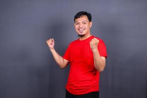 retrato de um homem asiático animado em pé com as mãos levantadas e olhando para câmera isolada em fundo cinza comemorando sucesso, vitória. foto