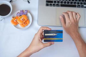 mão segurando o cartão de crédito para compras online no laptop durante comer café e biscoitos de halloween. feliz dia das bruxas, olá outubro, outono outono, conceito festivo, festa e feriado foto