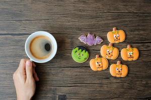 mão segurando a xícara de café durante a comer biscoitos engraçados de halloween. feliz dia das bruxas, truque ou ameaça, olá outubro, outono outono, tradicional, festa e conceito de férias foto