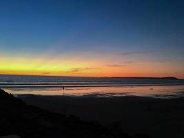 pôr do sol no mar, pôr do sol e noite ao mesmo tempo, pedras e areia em primeiro plano foto