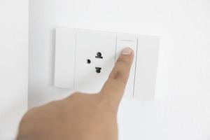 interruptor de luz de close-up de um dedo masculino ligará ou desligará um interruptor de luz com parede branca em casa. interruptor mecânico de plástico branco montado. energia, energia, economizar eletricidade, copie o espaço foto