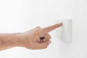 interruptor de luz de close-up de um dedo masculino ligará ou desligará um interruptor de luz com parede branca em casa. interruptor mecânico de plástico branco montado. energia, energia, economizar eletricidade, copie o espaço foto
