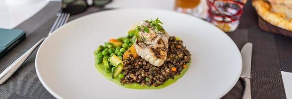 closeup comida gourmet e vista de mesa no restaurante. prato principal entre bife cozinha de peixe frito jantar fino, lentilha e legumes foto