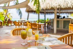 restaurante tropical ao ar livre com mesas de madeira, cadeiras sob palmeiras, coquetéis no resort de praia de luxo. férias de verão closeup coquetéis prontos para comer o conceito de família foto