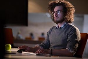 homem trabalhando no computador no escritório escuro foto