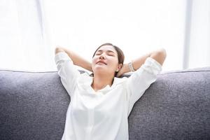 jovem mulher asiática sente-se relaxe no sofá na sala de estar. ela está dormindo ou tira uma soneca aliviando emoções negativas. foto