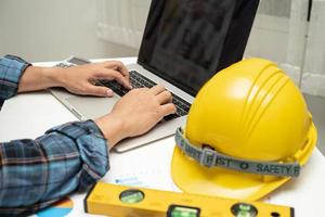 engenheiro asiático com planta de projeto de plano de casa arquitetônica, gráfico e capacete amarelo e ferramentas de construção de engenharia. foto