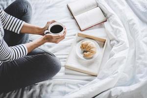 jovem na cama com um livro velho e uma xícara de café da manhã foto