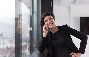 mulher elegante usando o celular pela janela no prédio de escritórios foto