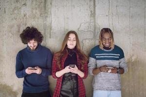 equipe de negócios multiétnica casual usando telefones celulares em frente a uma parede de concreto foto