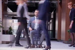 homem de negócios sentado na cadeira do escritório, grupo de pessoas passando foto