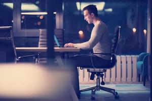 homem trabalhando no laptop no escritório escuro foto