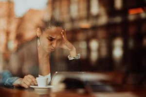 uma mulher latina senta-se em um café olhando ansiosamente para um tablet foto