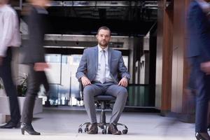 homem de negócios sentado na cadeira do escritório, grupo de pessoas passando foto