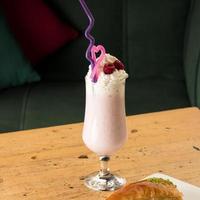 um smoothie de morango saudável em uma caneca com túbulos bebendo ao lado de baklava em uma mesa de madeira foto