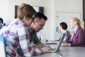 jovem casal de negócios trabalhando no laptop, grupo de empresários na reunião em segundo plano foto