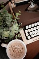close-up de uma xícara de café perto de uma máquina de escrever e uma planta foto
