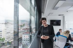 mulher elegante usando o celular pela janela no prédio de escritórios foto