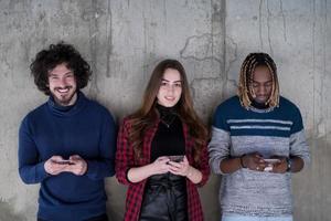 equipe de negócios multiétnica casual usando telefones celulares em frente a uma parede de concreto foto