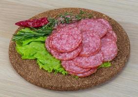 salame fatiado na placa de madeira e fundo de madeira foto