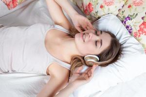 a jovem na cama ouvindo música, fones de ouvido foto