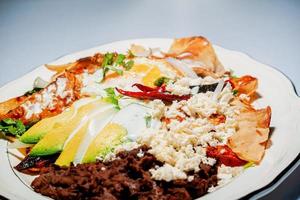 comida mexicana chilaquiles com molho vermelho, queijo, creme e pimenta em fundo vintage foto