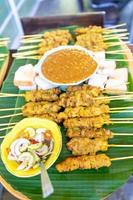 carne de porco satay grelhada, vara de comida popular tradicional da tailândia com madeira, cozida pronta para comer com molho específico ao lado. foto