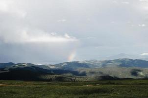 campo de grama com montanhas e um arco-íris à distância foto