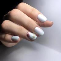 manicure branca feminina nas unhas contra um fundo escuro foto