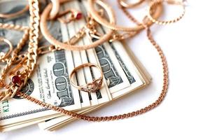 muitos anéis, brincos e colares dourados caros com grande quantidade de notas de dólar em fundo branco. loja de penhores ou joalheria foto