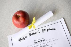 um diploma do ensino médio está na mesa com pequeno pergaminho e maçã vermelha. documentos de educação foto