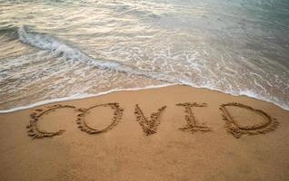 caligrafia covid na areia e onda de espuma na praia. conceito de coronavírus. foto