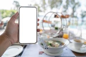 mãos de mulher segurando o telefone de maquete de tela em branco, pedir comida on-line conceito, fundo de café da manhã. foto