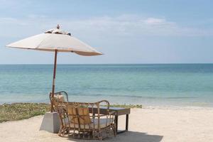 uma mesa com cadeiras e guarda-chuva para uma refeição romântica na praia, céu e mar ao fundo.