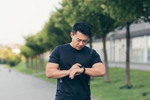 atleta asiático masculino, cansado depois de uma corrida matinal, corre no parque perto do estádio foto