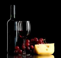 garrafa e copo de vinho tinto com uvas e queijo foto