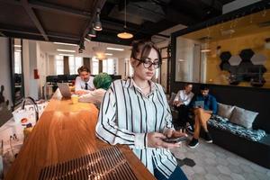 empresária com óculos usando telefone celular no interior do escritório de plano aberto de inicialização moderna. foco seletivo foto