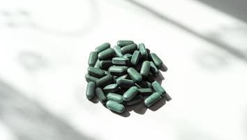 pílulas de chlorella, spirulina, grama de cevada em fundo branco com sombras escuras close-up e suplemento nutricional de padrão de sombra, superalimento de desintoxicação foto