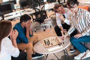 grupo multiétnico de empresários jogando xadrez enquanto faz uma pausa na área de relaxamento no escritório de inicialização moderno foto