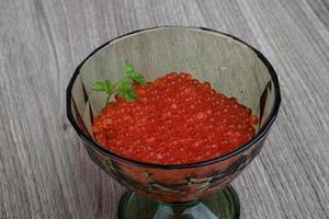 caviar vermelho em uma tigela sobre fundo de madeira foto