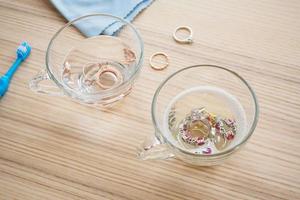 limpeza de anel de diamante de joias com copo de água quente e detergente líquido no fundo da mesa de madeira foto