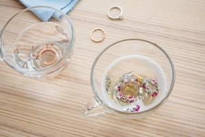 limpeza de anel de diamante de joias com copo de água quente e detergente líquido no fundo da mesa de madeira foto