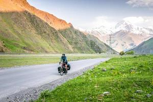 bicicleta de ciclista masculino caucasiano em turnê nas montanhas kazbegi do cáucaso e pico kazbek ao fundo. viajar pelo Cáucaso. ciclo ao redor do mundo foto