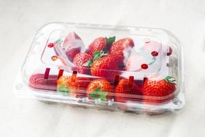 morangos frescos doces em recipiente plástico em cima da mesa. recipiente de caixa plástica de loja de supermercado com frutas vermelhas. foto