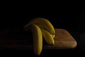 bananas amarelas maduras em uma placa de madeira em um fundo preto foto